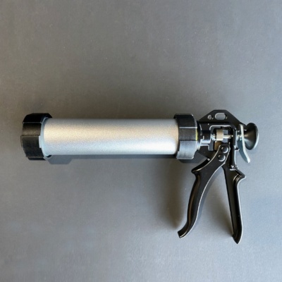 Pistola aplicadora de silicone prateada com empunhadura preta sobre superfície cinza