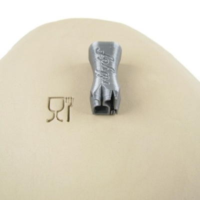 Peça metálica cinza com gravação 'fidget' sobre superfície bege clara com símbolos gravados