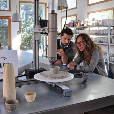 Máquina de moldagem de cerâmica em ambiente laboratorial com duas pessoas observando.