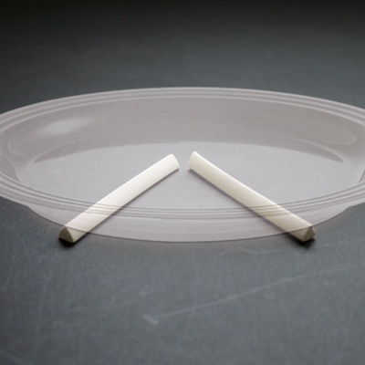 Prato oval de vidro transparente com detalhes gravados na borda e dois pedaços de giz branco no centro