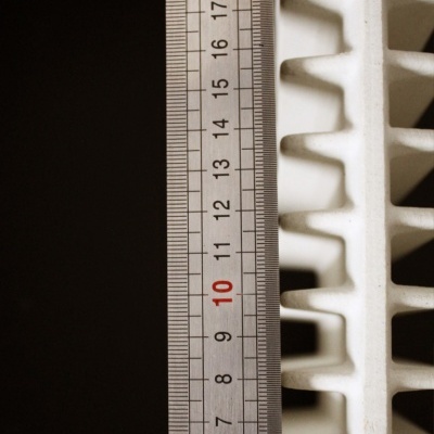 Régua metálica ao lado de peça branca com ranhuras em fundo escuro