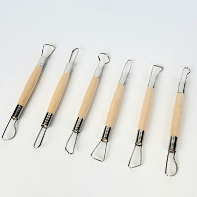 Seis ferramentas de modelar com cabos de madeira e pontas de metal em fundo branco