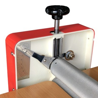 Máquina metálica vermelha com cilindro prateado texturizado numa mesa de madeira.