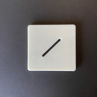 Objeto quadrado branco com ranhura diagonal sobre superfície escura