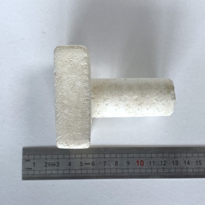 Peça branca em forma de T com textura rugosa, ao lado de régua metálica sobre superfície branca