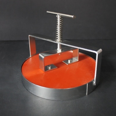 Prensa redonda metálica com base laranja e estrutura prateada