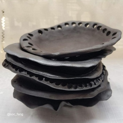 quatro pratos pretos de cerâmica empilhados com bordas onduladas e perfurações