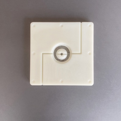 Dispositivo quadrado branco com botão redondo metálico central sobre fundo cinzento