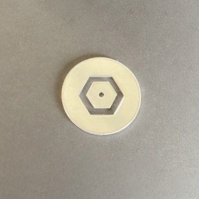 Disco redondo creme com recorte hexagonal no centro sobre superfície cinzenta