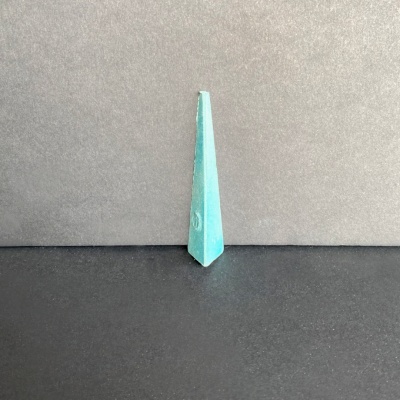 Objeto decorativo pirâmide verde-azulada em superfície preta e fundo cinzento