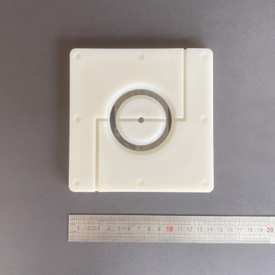Peça quadrada branca com círculo transparente e régua metálica ao lado