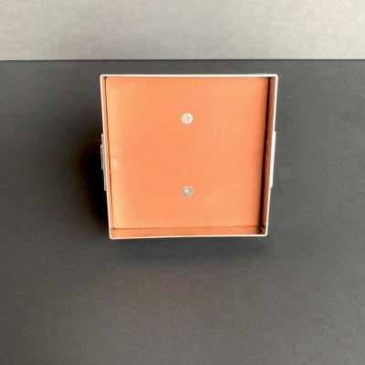 Caixa quadrada castanha clara aberta com interior forrado e duas pedras brilhantes no centro.