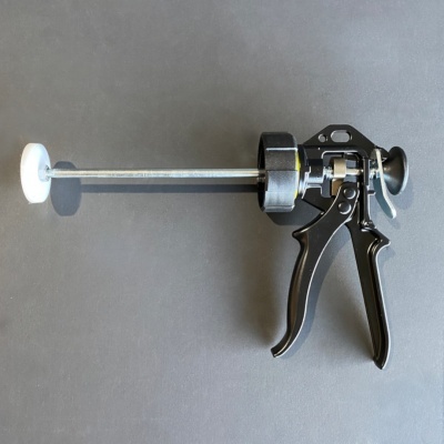 Ferramenta manual preta com haste longa metálica e disco branco em fundo cinzento