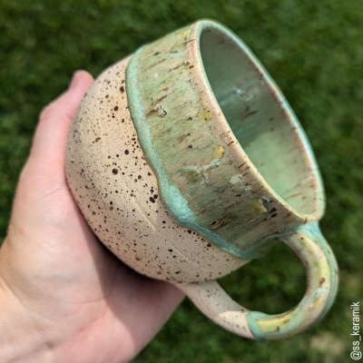 Caneca artesanal de cerâmica bege e verde com textura rústica ao ar livre