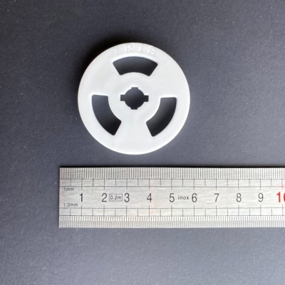 Disco plástico branco com inscrição R15 junto a régua metálica numa superfície preta