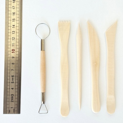 Conjunto de ferramentas de escultura em madeira clara ao lado de régua metálica.
