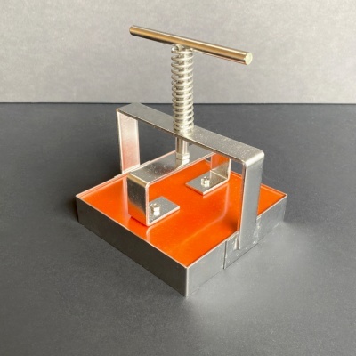 Aparelho de pressão metálico prateado com base laranja e parafuso T no topo