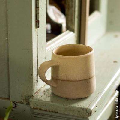 Caneca de cerâmica bege em superfície de madeira verde clara envelhecida