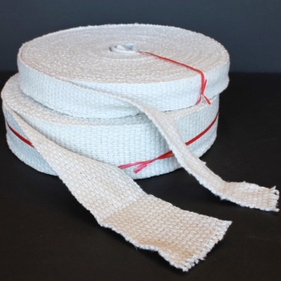 Bobinas de fita têxtil branca com fios vermelhos, sobre superfície preta