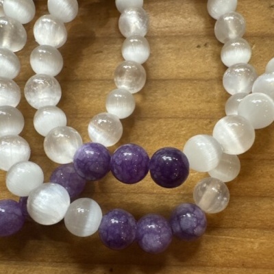 Pulseiras com contas brancas translúcidas e roxas numa superfície de madeira clara