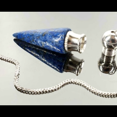 Pêndulo de cristal azul com base metálica e corrente prateada sobre superfície espelhada