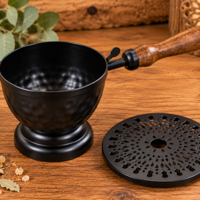Utensílio de cozinha preto com cabo de madeira e tampa perfurada sobre mesa de madeira