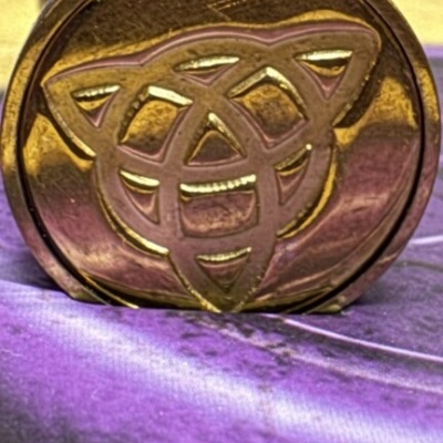 Selo de metal dourado com desenho entrelaçado e cabo de madeira sobre tecido roxo