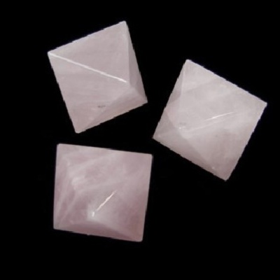 Três pedras de quartzo rosa lapidadas em forma de pirâmide em fundo preto
