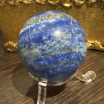 Esfera azul em suporte transparente sobre madeira e fundo dourado