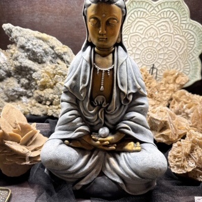 Estátua de Buda meditando em cinzento e dourado com minerais ao redor