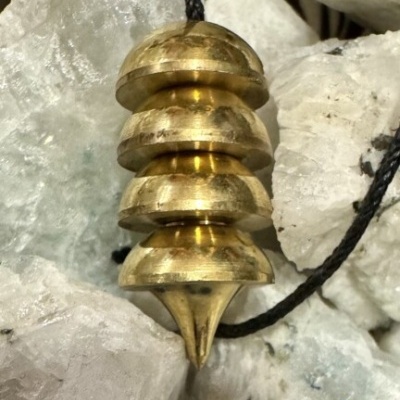 Pêndulo dourado com discos empilhados e cordão preto sobre pedras translúcidas