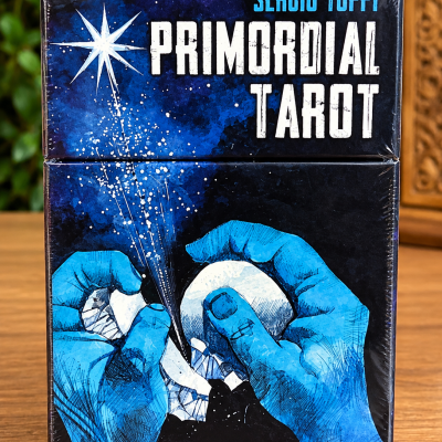 Caixa de tarot Primordial Tarot com ilustração de mãos azuis segurando ovo partido