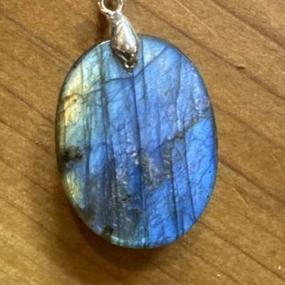 Pingente oval em pedra labradorita azul com argola prateada sobre madeira