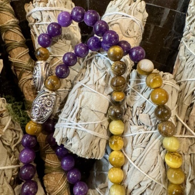 Pulseiras de pedras roxas e amarelas sobre feixes de folhas secas amarradas
