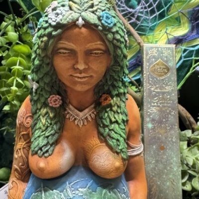 Estátua de mulher grávida com barriga pintada como planeta Terra em ambiente com plantas