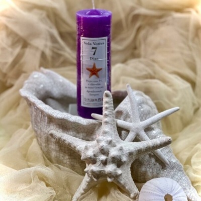 Vela votiva roxa em concha decorativa branca com estrelas-do-mar e ouriço-do-mar em tecido bege.