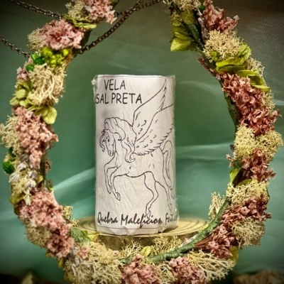 Vela branca com desenho de pégaso e texto, circundada por guirlanda de flores secas rosa e verde.