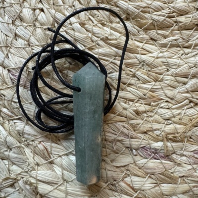 Colar com pendente de pedra verde facetada em corda preta sobre esteira de palha