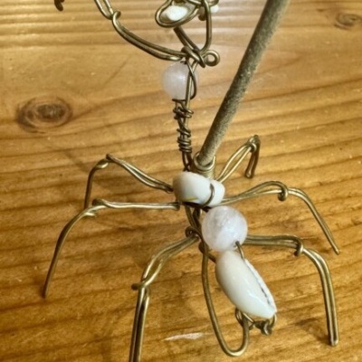 Escultura de aranha feita com arame dourado e pedras brancas sobre mesa de madeira