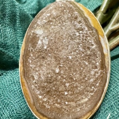 Pingente oval com pedra natural castanha e cristais sobre tecido verde