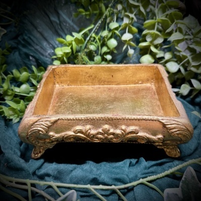 Tabuleiro retangular dourado com relevo decorativo sobre tecido azul e folhas verdes
