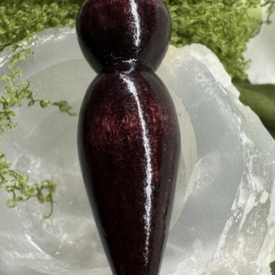 Figura feminina esculpida polida castanha avermelhada sobre cristais brancos com vegetação verde.