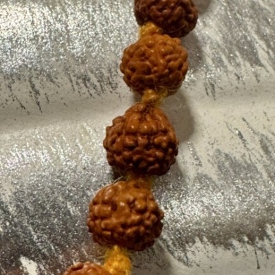 Colar de contas castanhas com fio amarelo sobre superfície metálica prateada