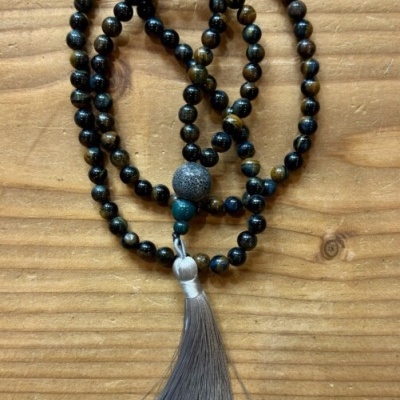 Colar de contas castanho e preto com tassel cinzento sobre madeira clara