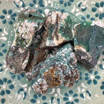 Pedras rústicas verdes e brancas sobre prato decorativo verde com padrão branco e azul