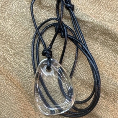 Colar com pendente de vidro transparente e cordão preto sobre tecido castanho