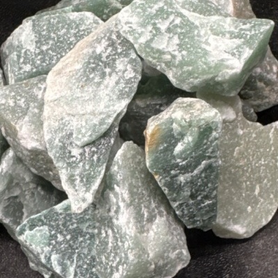 Pedras brutas verdes e brancas em superfície escura.