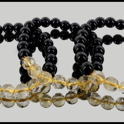 Três pulseiras de contas pretas e transparentes amarelas sobre superfície espelhada cinza.