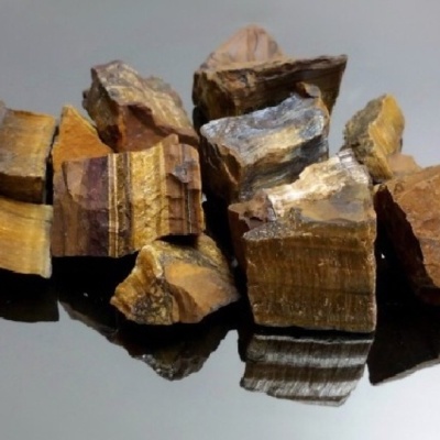 Pedras brutas castanhas e douradas com textura estriada num fundo preto refletor
