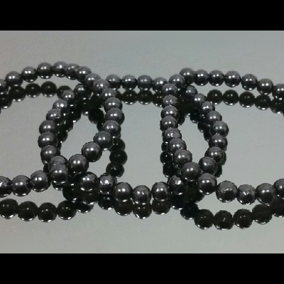 Quatro pulseiras de contas negras brilhantes em superfície cinza refletora